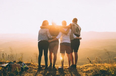 four person standing on a cliff in front of sun